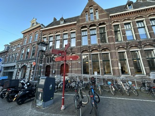 Historic brick townhouses and a red directional signpost above rows of parked bicycles on a European river town street Historic brick townhouses and a red directional signpost above rows of parked bicycles on a European river town street