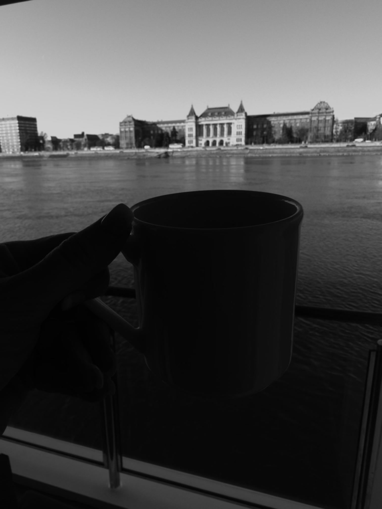 Morning coffee held at a river cruise stateroom window overlooking the Danube and Budapest riverfront architecture. Morning coffee held at a river cruise stateroom window overlooking the Danube and Budapest riverfront architecture.