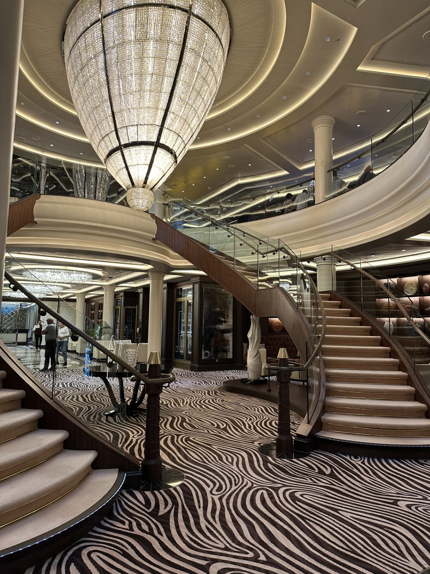Grand atrium aboard a Regent Seven Seas ship with a curved double staircase and a crystal chandelier